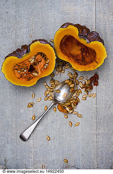 High angle close up of silver tablespoon and purple pumpkin with orange flesh cut in half.