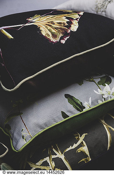 High angle close up of stack of three cushions in black and grey with floral patterns.