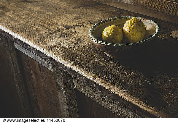 High angle close up of two lemons in earthenware bowl on vintage wooden kitchen cupboard.