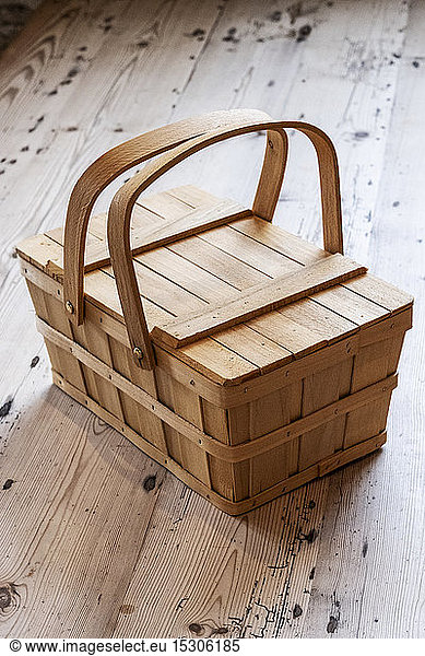 High angle close up of wooden picnic basket on wooden floor.