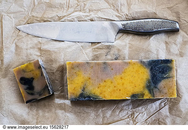 High angle close up of yellow and black homemade bar of soap and kitchen knife.