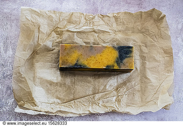 High angle close up of yellow and black homemade bar of soap on brown paper.