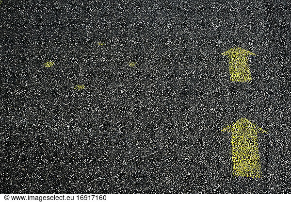 High angle close up of yellow arrow symbols painted on asphalt ground.