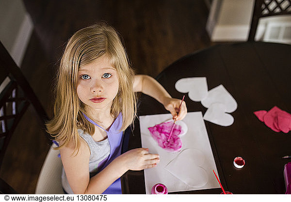 High angle portrait of girl making heart shapes of papers on table at home