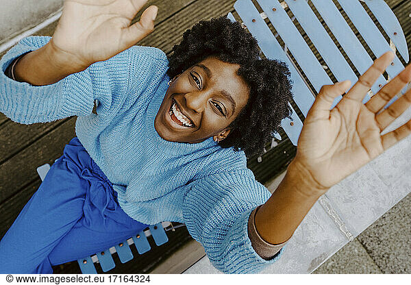 High angle portrait of smiling woman sitting on deck chair in balcony