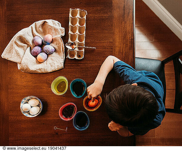 High angle shot of young boy dying Easter eggs at a wooden table.