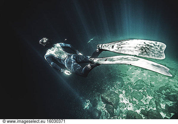High angle underwater view of diver wearing wet suit and flippers  sunlight filtering through from above.