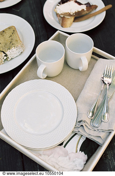 High angle view of a tray with mugs  plates and cutlery  pastries.