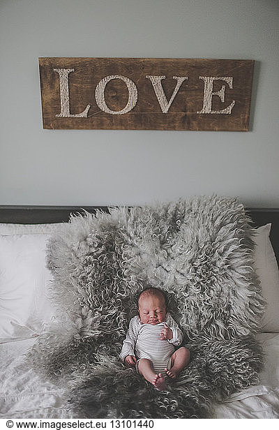 High angle view of baby boy sleeping on fur rug in bedroom with love decor on wall