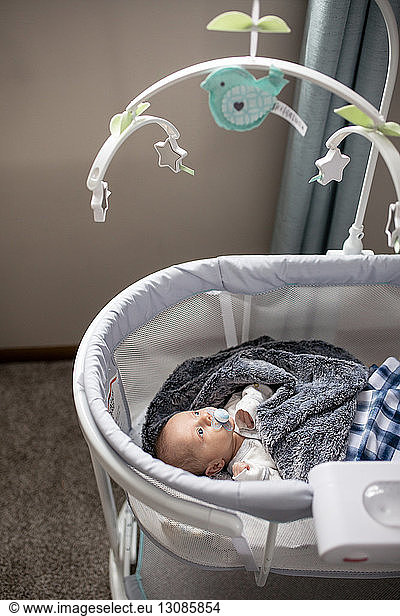 High angle view of baby boy sucking pacifier while looking at hanging mobile in crib