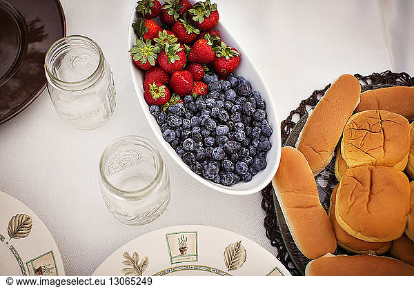 High angle view of berries and breads with mason jars served on table