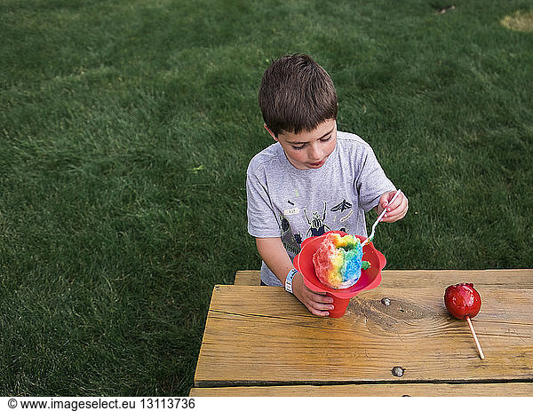 High angle view of boy eating flavored ice while sitting on bench at park