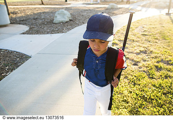 High angle view of boy in baseball uniform with backpack walking in yard