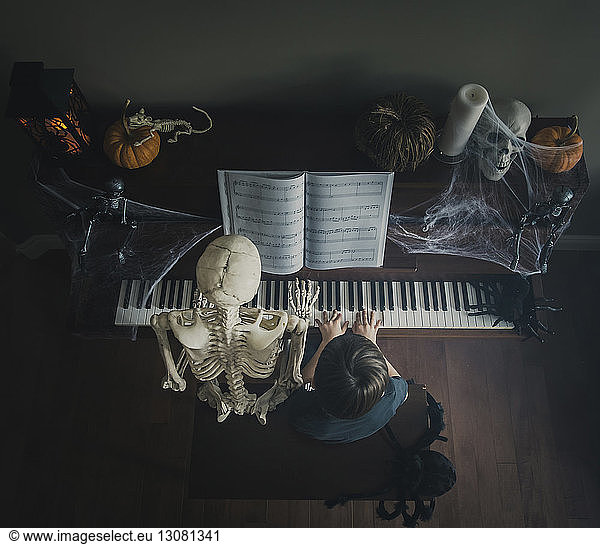 High angle view of boy playing piano while sitting by skeleton during Halloween