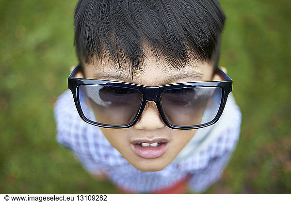High angle view of boy wearing oversized black sunglasses while standing on field at park