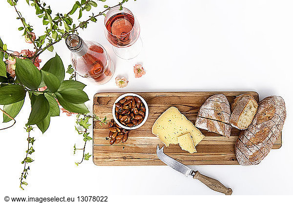 High angle view of bread with cheese and almonds on cutting board by wine over white background