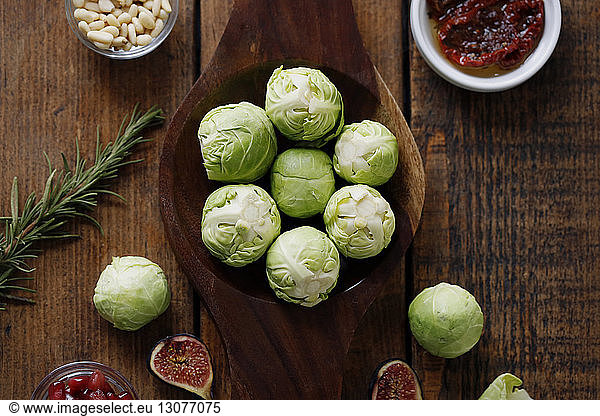 High angle view of Brussels sprouts with rosemary and fruits and pine nuts on wooden table