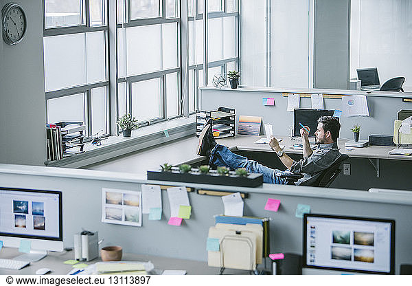 High angle view of businessman reading document while relaxing on chair in office