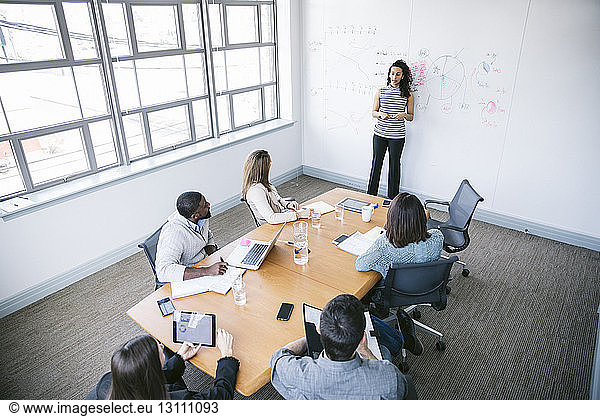 High angle view of businesswoman explaining data while standing by whiteboard in board room