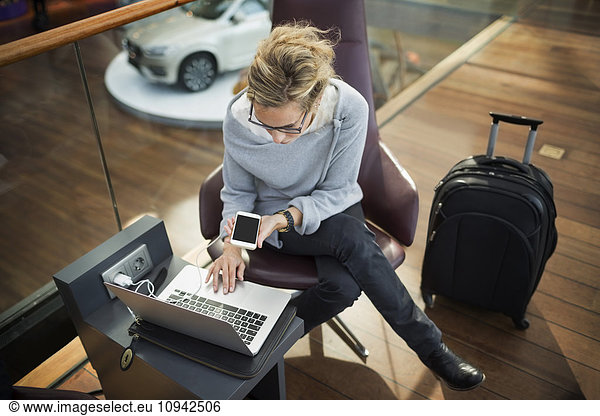High angle view of businesswoman using laptop and smart phone at airport lobby