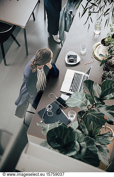 High angle view of businesswoman with laptop and mobile phone sitting at desk in office