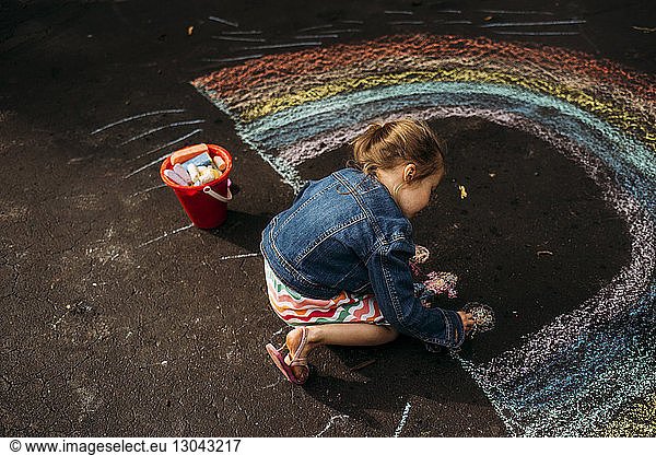 High angle view of carefree girl drawing rainbow on asphalt