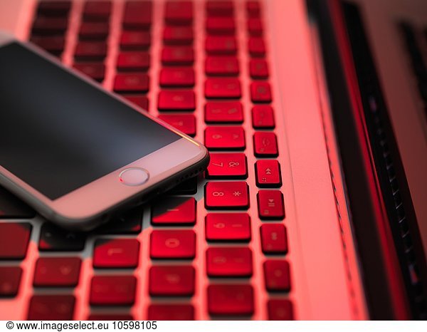 High angle view of cellular phone on computer keyboard in red lighting