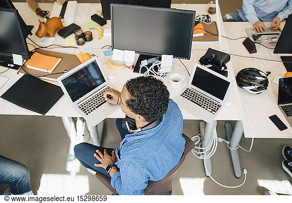 High angle view of computer hacker with laptop sitting at desk in office
