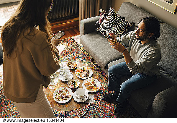 High angle view of couple photographing breakfast in hotel room
