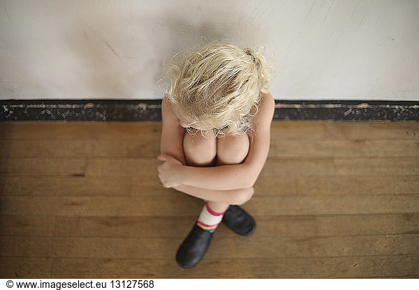 High angle view of depressed girl hugging knees while sitting on floor at home