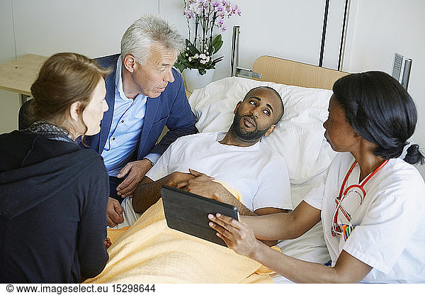 High angle view of doctor discussing over digital tablet with patient and family in hospital ward