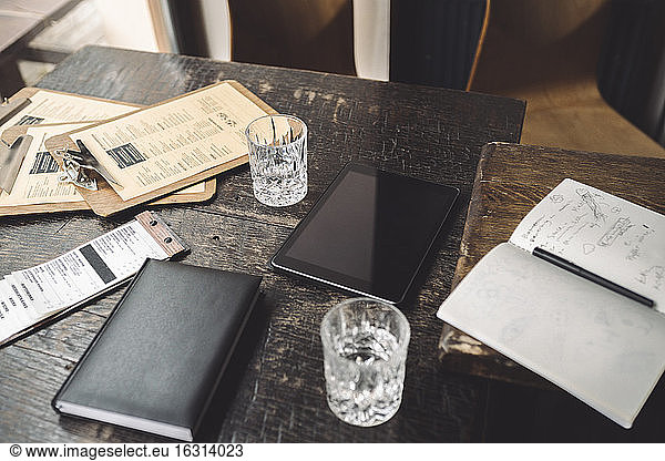 High angle view of drinking glass with diary and digital tablet on table in restaurant