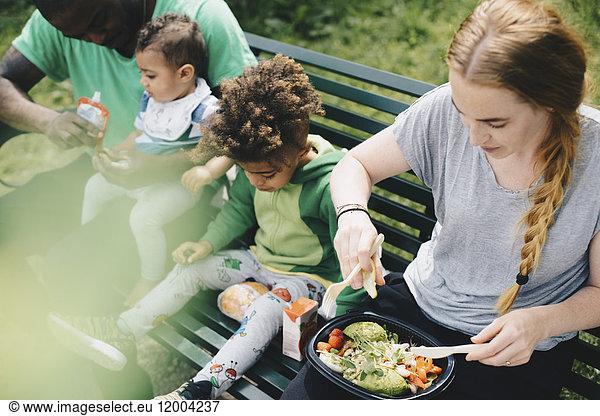 High angle view of family having food while sitting on bench at park