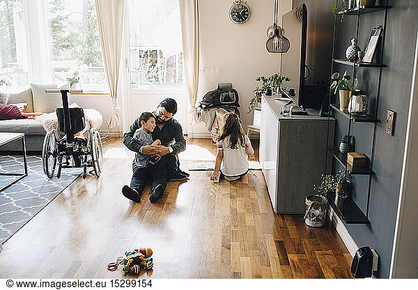 High angle view of father holding autistic son while sitting by daughter on floor at home
