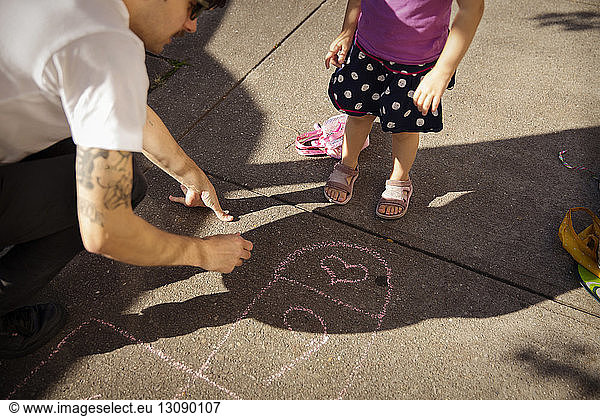 High angle view of father with daughter drawing on footpath
