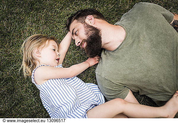 High angle view of father with daughter lying on grassy field at yard