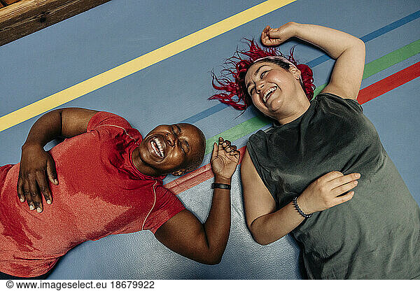 High angle view of female athletes laughing while lying on safety mat at sports court