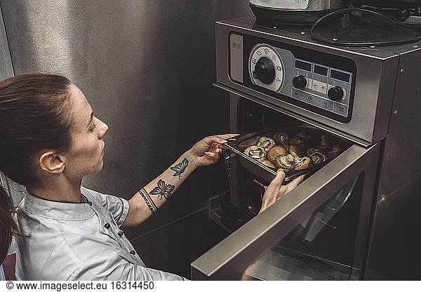 High angle view of female chef baking mushrooms in oven