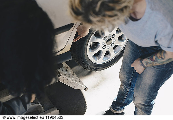 High angle view of female customer showing damaged car to mechanic at repair shop