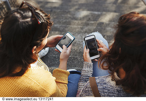 High angle view of female friends using smart phones while sitting on steps