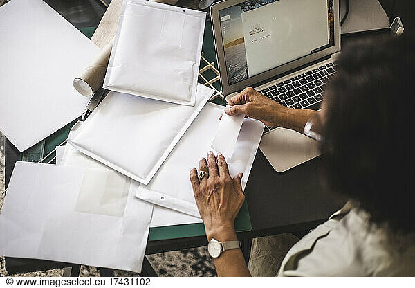 High angle view of female owner labeling on envelope while working in office