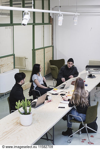 High angle view of four entrepreneurs discussing at desk in creative office