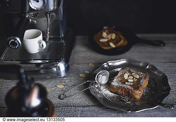 High angle view of French toasts with almonds served in plate by espresso maker on wooden table