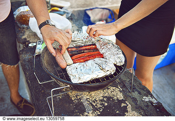 High angle view of friends preparing sausages on barbeque grill