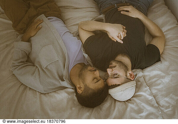 High angle view of gay couple lying on bed with eyes closed resting at home