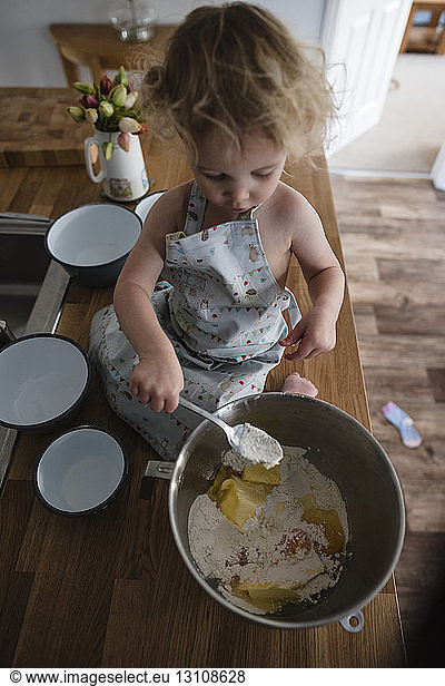 High angle view of girl mixing batter in bowl while sitting on kitchen counter