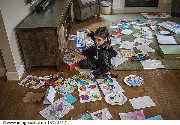 High angle view of girl painting on papers while sitting on floor at home