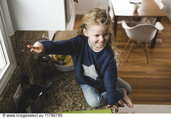 High angle view of girl pointing while sitting on kitchen counter at home
