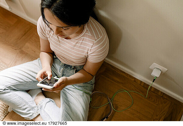 High angle view of girl using smart phone while sitting by wall at home