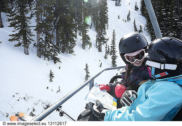 High angle view of girls reading map while riding on ski lift